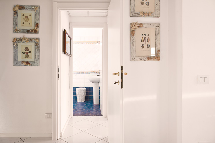 # Ulisse Albiati fotografo architettura interni: fotografia immobiliare disimpegno, con accesso al bagno di servizio di una villetta al mare. Ambiente luminoso con dominanti di colore blu e bianco, in stile marinaro. Zona Cinquale nei pressi del Forte dei Marmi, riviera della Versilia.