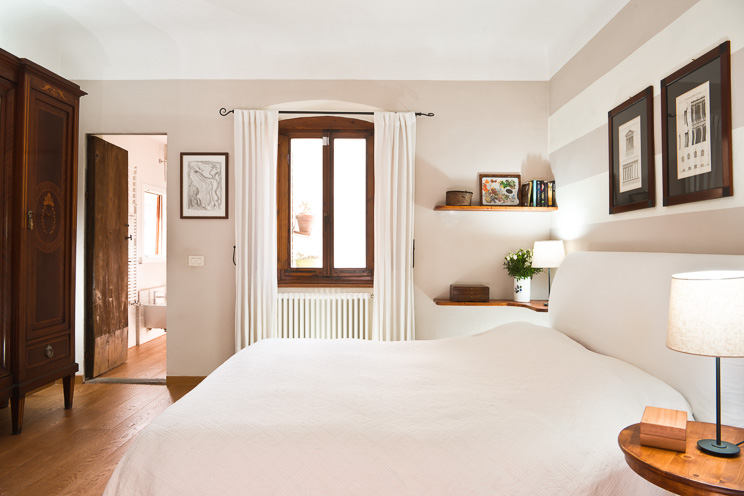 # Ulisse Albiati fotografo architettura interni: fotografia immobiliare camera da letto matrimoniale. Stile sobrio ed elegante, con autentico parquet in legno di ciliegio. Finestra sul cortile interno e accesso al bagno di servizio. Attico in zona Greve in Chianti, Toscana.