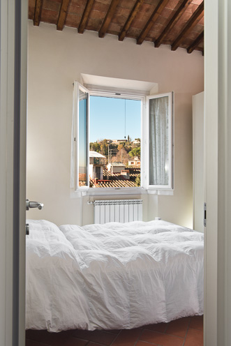 # Ulisse Albiati fotografo architettura interni: fotografia camera matrimoniale di un bed and breakfast. Pavimento in cotto e soffitto con travi a vista. Finestra con affaccio sulle colline di Bellosguardo. Attico B&B in zona viale Petrarca a Firenze, Toscana.