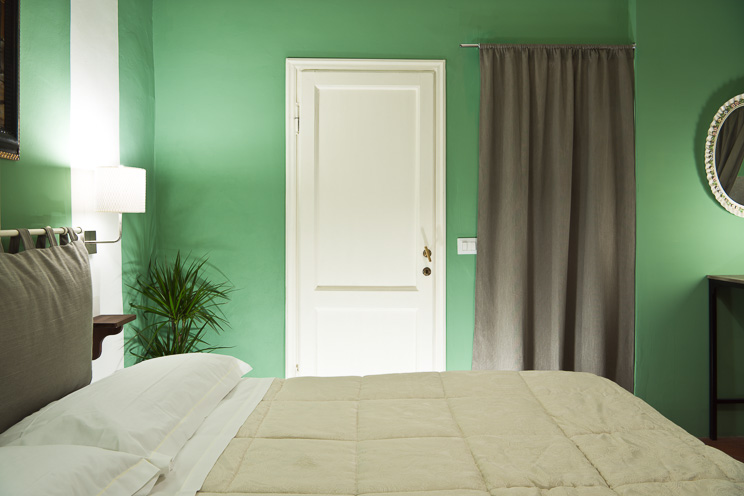 # Ulisse Albiati fotografo architettura interni: fotografia stanza da letto di un bed and breakfast. Porta di accesso al bagno di servizio. Pareti di colore verde. B&B, monolocale, ambiente unico e aperto in zona via delle Caldaie, nei pressi di piazza Santo Spirito a Firenze, Toscana.